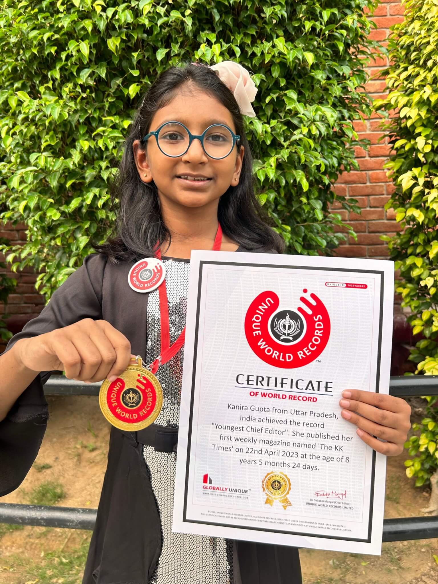 Kanira Gupta, the world's youngest chief editor of a magazine - The KK Times, smiling and showing her certificate, medal and badge after breaking the record.